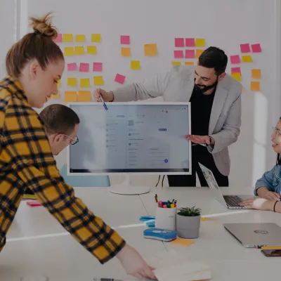 This is a photo of a team in a meeting room referring to a computer monitor doing a workshop with Dr. Liz Wilson from Include Inc. - Diversity and inclusion expert consultant